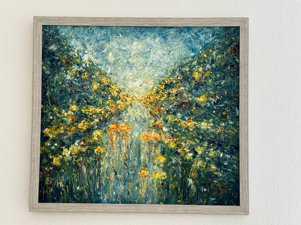 Dipinto impressionista di un sentiero nel bosco con fiori gialli e fogliame verde contro un cielo blu, incorniciato su un muro bianco: il tocco perfetto per il tuo appartamento in affitto.